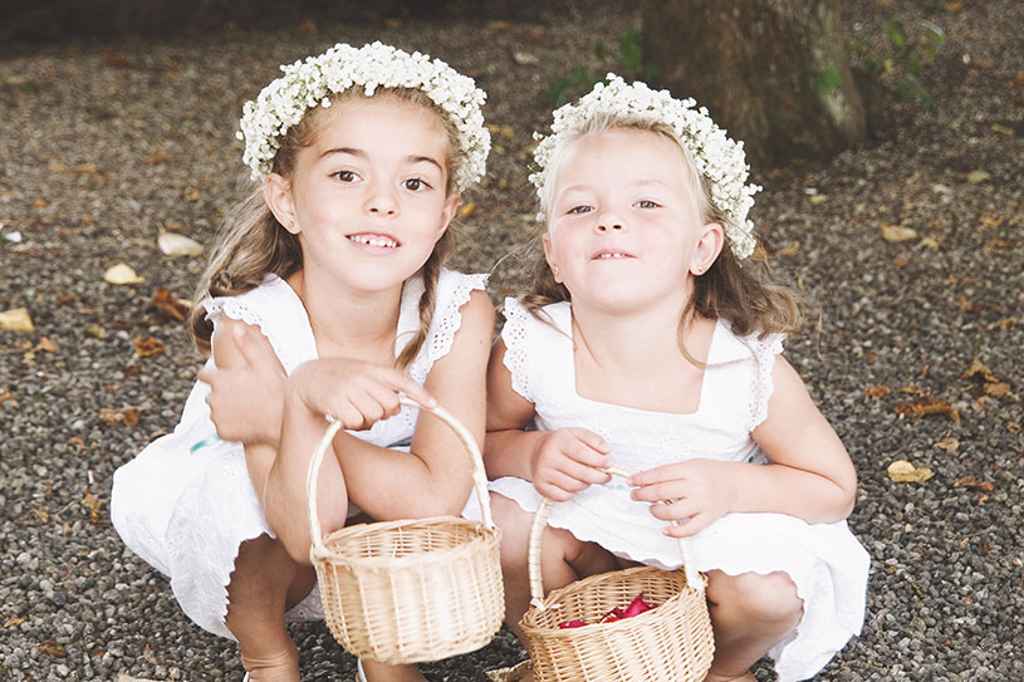 Prikupni deklici v beli obleki, s cvetlično kronico in košarico v rokah na poroki, kot trosilki cvetja. Foto: Storija weddings