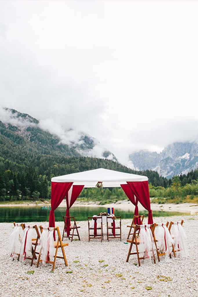 Intimna postavitev poročnega obreda na plaži jezera Jasna v Kranjski gori. Postavitev je sestavljena iz bele pagode z rdečimi stranicami, stoli dekorirani z rdečimi in belimi trakovi ter mize za matičarja. Foto: Alen Karupovič Photography