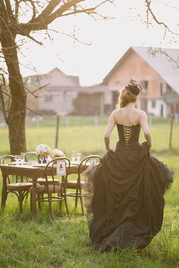 Nevesta v prekrasni črni poročni obleki z odprtim hrbtom hodi okrog poročnega omizja, na katerim je cvetje v zlato beli kombinaciji v črnih vazah. Foto: Urška & Domen Photography