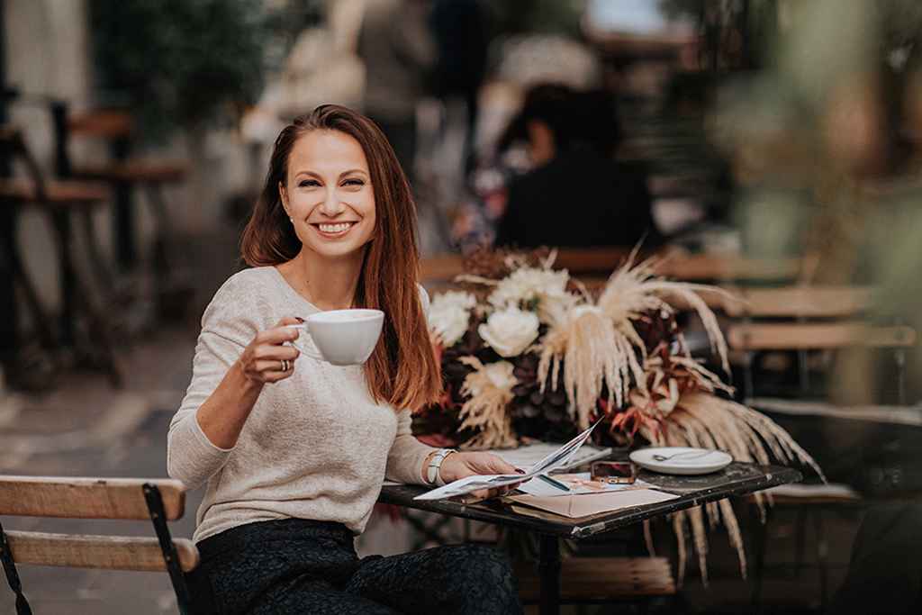 Nasmejana organizatorka porok Petra Starbek sedi v ljubljanski kavarni in čaka na par s kavo v roki. Foto: Ana Gregorič Photography