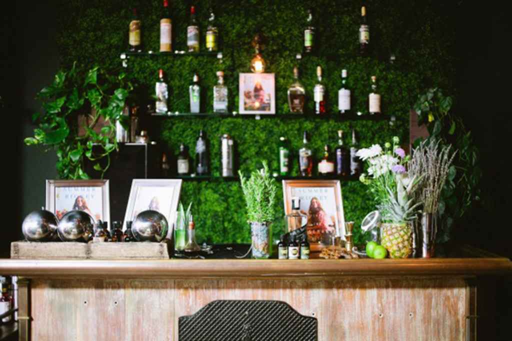 Elegantna barska mizica, narejena iz lesa ter steno iz zelenja, na kateri so lepo zložene alkoholne pijače. Foto: Liz Wang Photography