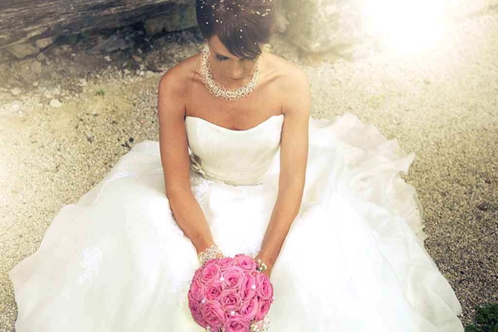 Nevesta z diamantno verižico sedi na tleh in v rokah drži roza poročni šopek. Foto: arhiv Zlatarnica