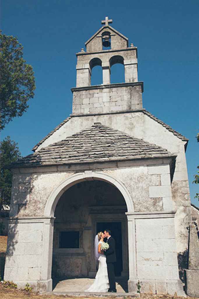 Nevesta v boho poročni obleki in ženin objeto stojita pred majhno toskansko cerkvico. Foto: Alen Karupovič Photography