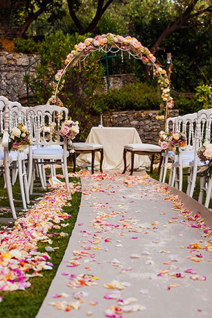 Romantična postavitev poročnega obreda s polkrožnim cvetličnim obokom ter posutim cvetjem ob stolih. Foto: Storija weddings