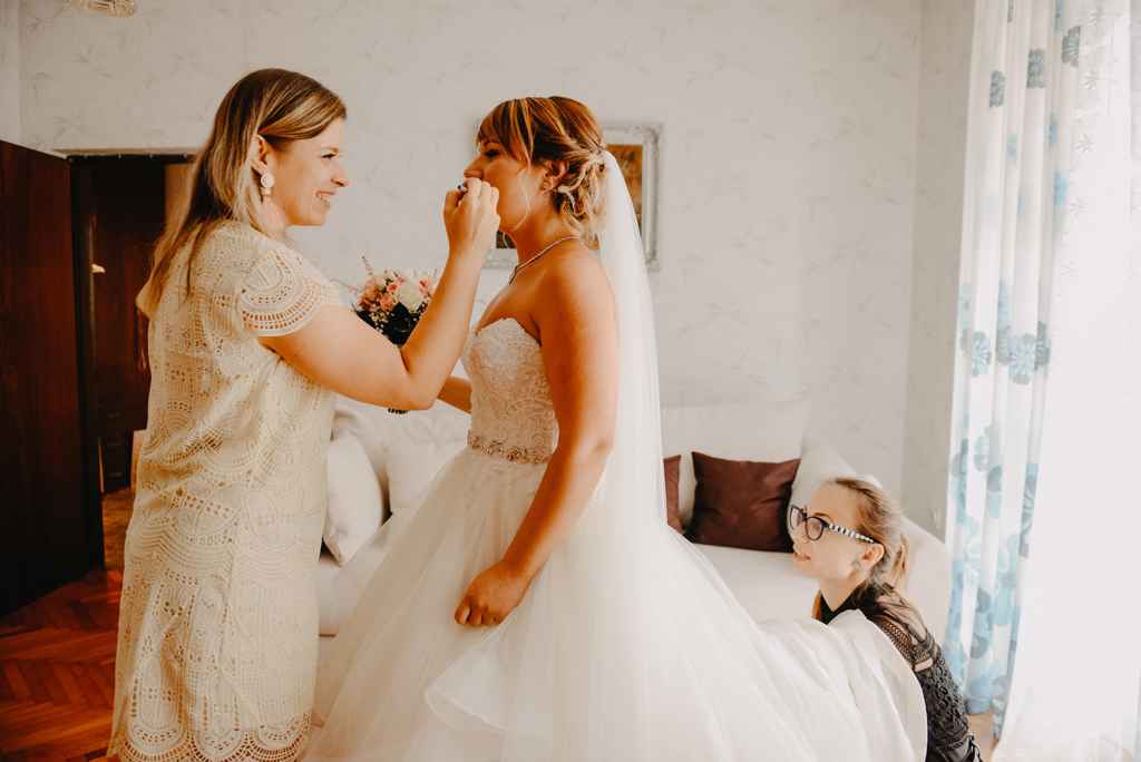 Organizator porok Petra Starbek pomaga nevesti pri oblačenju njene princes poročne obleke. Foto: Moj Fokus Photography