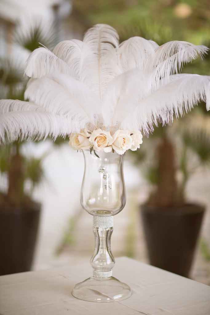Poročni cvetlični aranžma, postavljen v visoko stekleno vazo. Sestavljen je iz bež vrtnice, belega perja ter kristalov. Foto: Ana Gregorič Photography