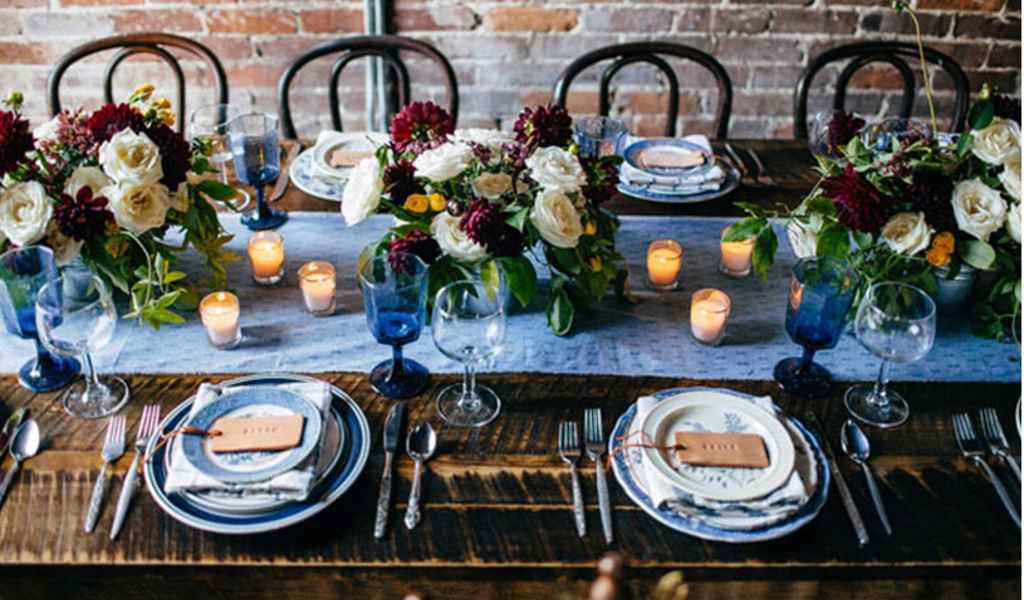 Poročno omizje je sestavljeno iz: starinske mize na kateri je moder svilen tekač, pisano cvetje, svečke, modri in beli kozarci, srebrni pribor, krožniki z modrimi detajli, imenske kartice ter beli prtički z modrim vzorcem. Foto: Tiffani Jones