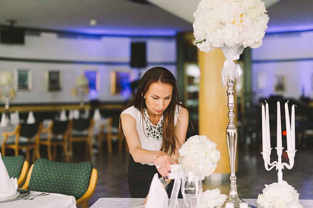 Organizatorka porok Petra Starbek pripravlja poročno omizje v restavraciji Arboretum z belim cvetjem in visokimi srebrnimi svečniki. Poroka košarkarja Jake Klobučarja. Foto: Nastja Kovacec Photography