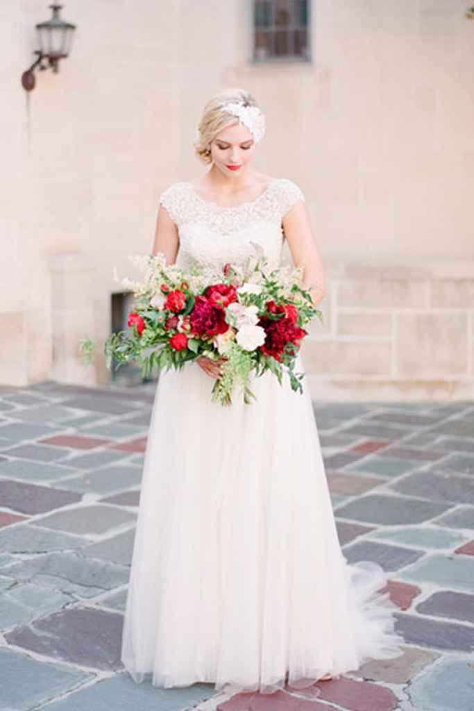 Nevesta v beli poročni obleki drži v rokah moderen rdeč poročni šopek. Foto: Koman Photography