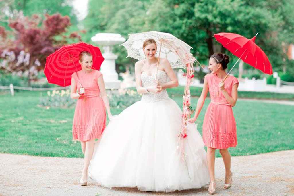 Nevesta si je izbrala poročni šopek, narejen iz čipkastega dežnika in padajočega cvetja na eni strani. Poleg nje stojita dve družici v rdeči obleki in majhnim šopkom. Foto: Jordan Brittley