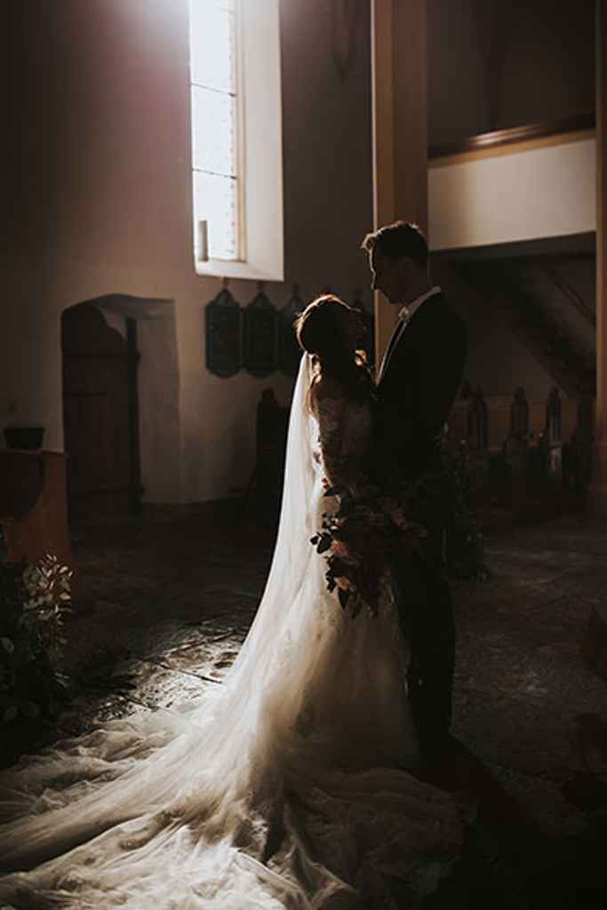 Nevesta v prekrasni sanjski poročni obleki s 3-metrsko vlečko objema ženina med poročnim fotografiranjem v cerkvi. Foto: Ana Gregorič Photography