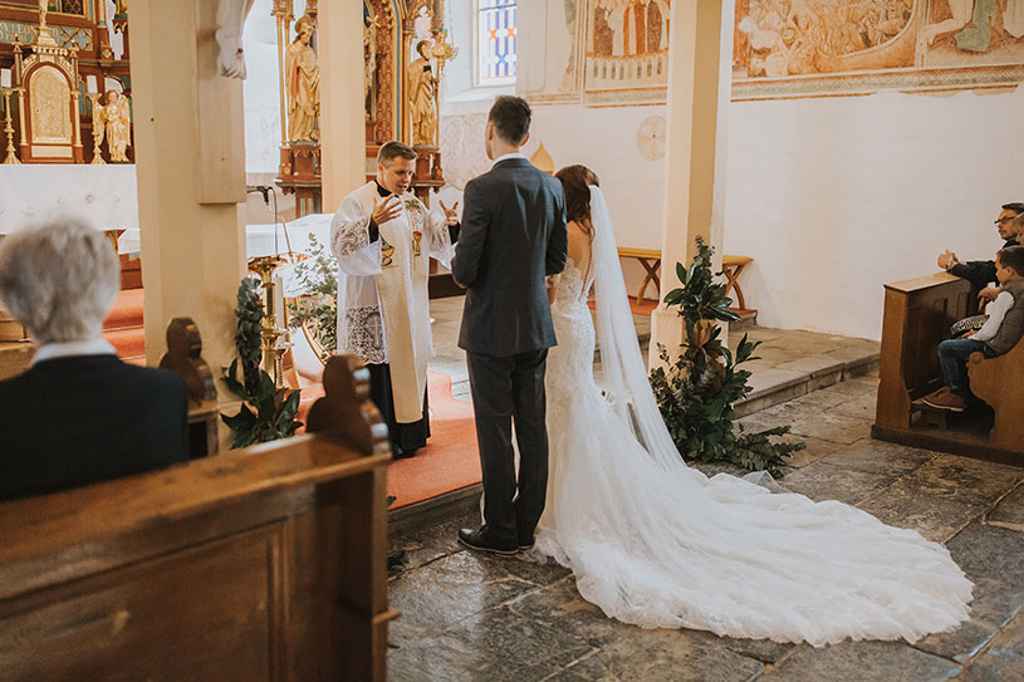 Nevesta v čudoviti prekrasni obleki in ženin v po meri narejeni obleki stojita med intimnim cerkvenim obredom. Foto: Ana Gregorič Photography