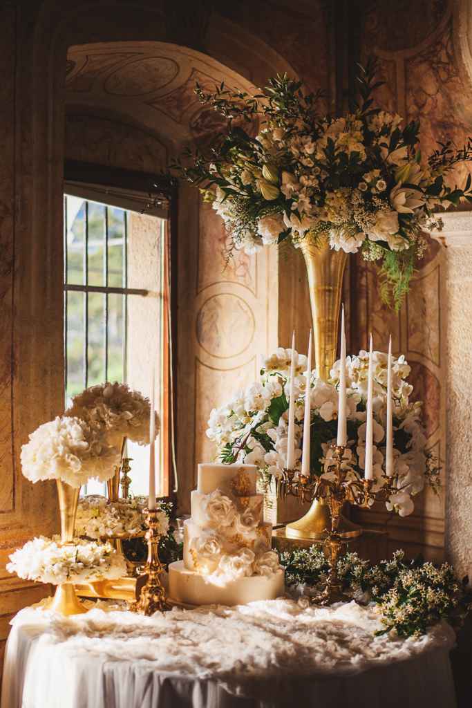 Prekrasno dekorirana miza z belo zelenim cvetje, svečami na zlatih svečnikih je bila središče pozornosti za belo z zlatom posuto poročno torto. Foto: Aleks in Irena Kus wedding photography
