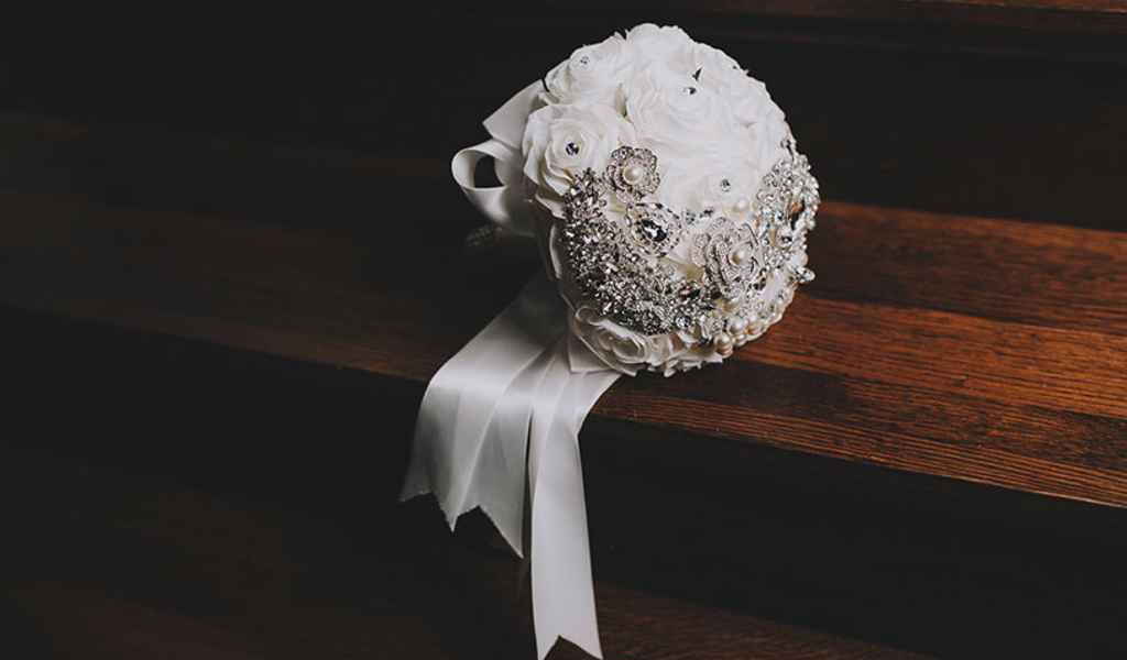 Prekrasen, okrogel, bel ter s srebrnimi broškami okrašen poročni šopek. Foto: Aperturia weddings