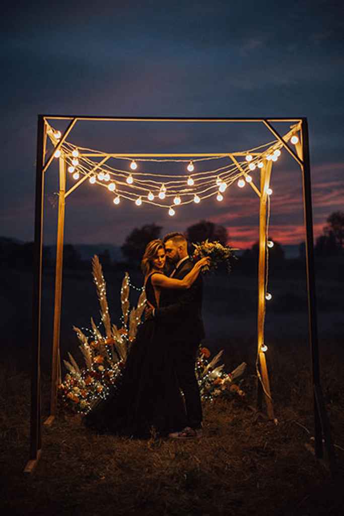 Coolfotr in coolmamacita zaljubljeno stojita pred boho cvetličnim obokom iz cvetličarne Sanjski šopek nad katerim visijo garden lights. Foto: JS Oblikovanje