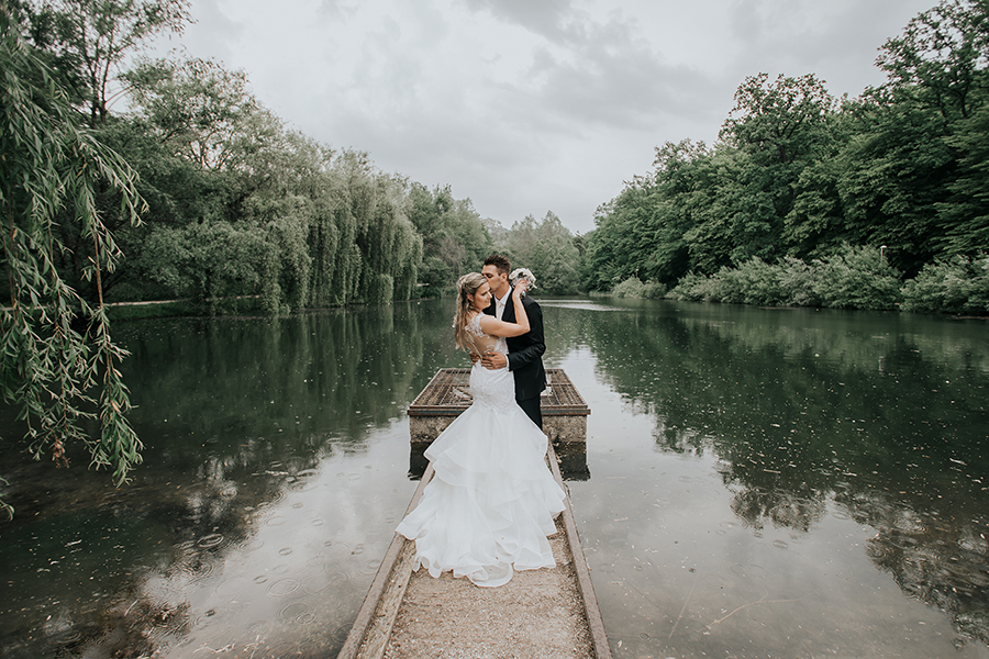 Ženin in nevesta stojita na pomolu jezera ob poročni lokaciji Tri lučke. Ženin v po meri narejeni obleki objema nevesto v prečudoviti beli dolgi obleki. Par je sproščen in zadovoljen, saj za njuno poroko skrbi vrhunska organizatorka porok Petra Starbek.